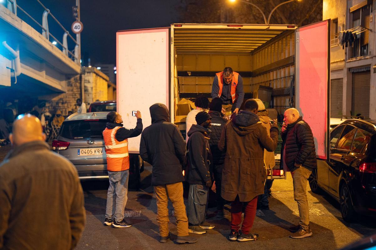 Voluntarios de distintas entidades privadas reparten comida para la cena de Nochebuena bajo la autopista C-31, donde aún duermen decenas de personas desalojadas del antiguo instituto B9