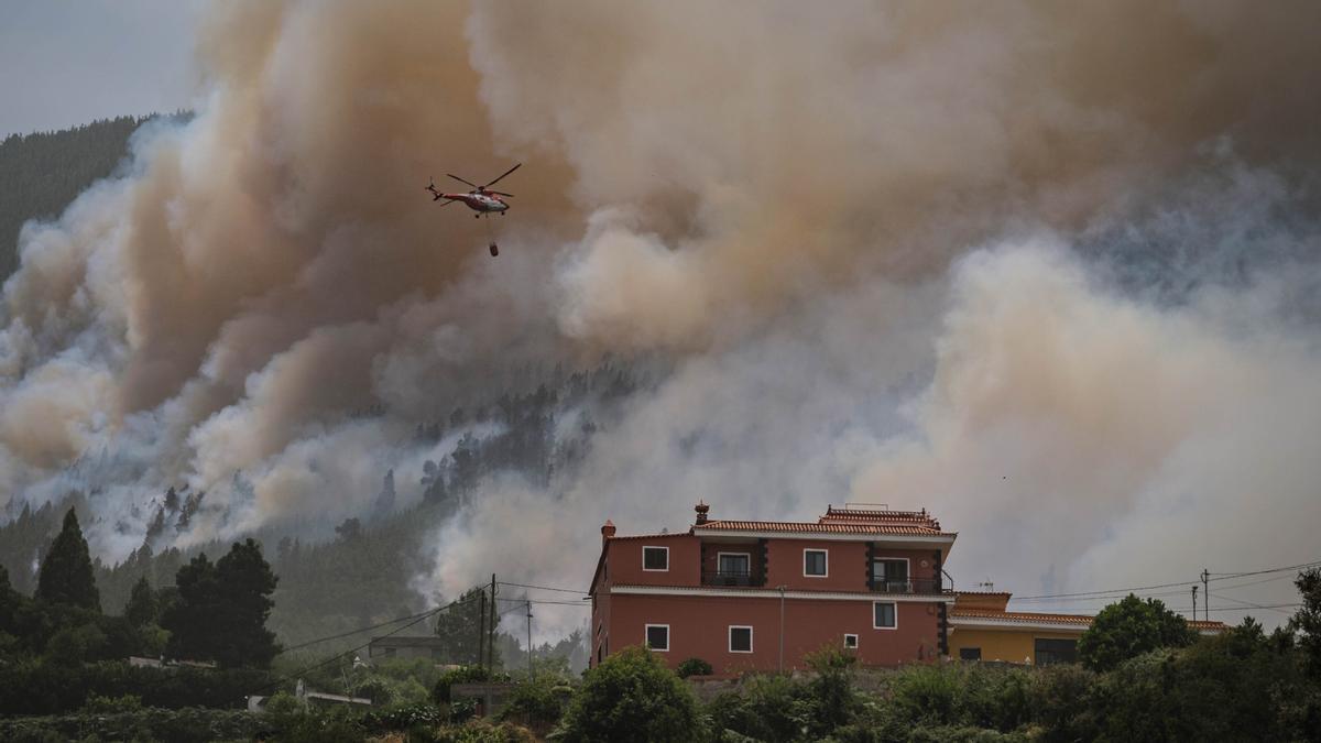 Un helicóptero lanza agua sobre el incendio, muy pegado a una vivienda.