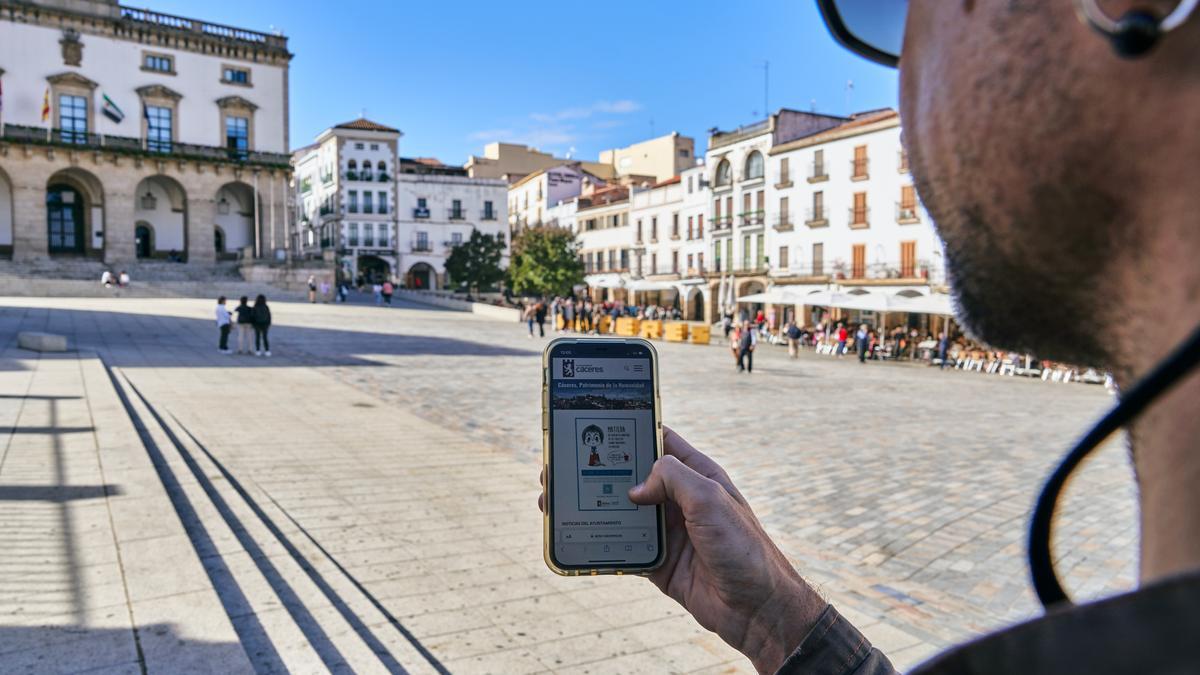 Un usuario mira la página web del Ayuntamiento de Cáceres en la plaza Mayor. Al fondo, el consistorio.