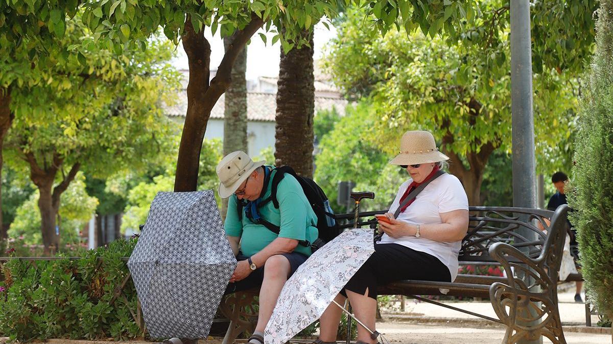 Dos personas se alivian del calor cordobés con sombreros y paraguas.