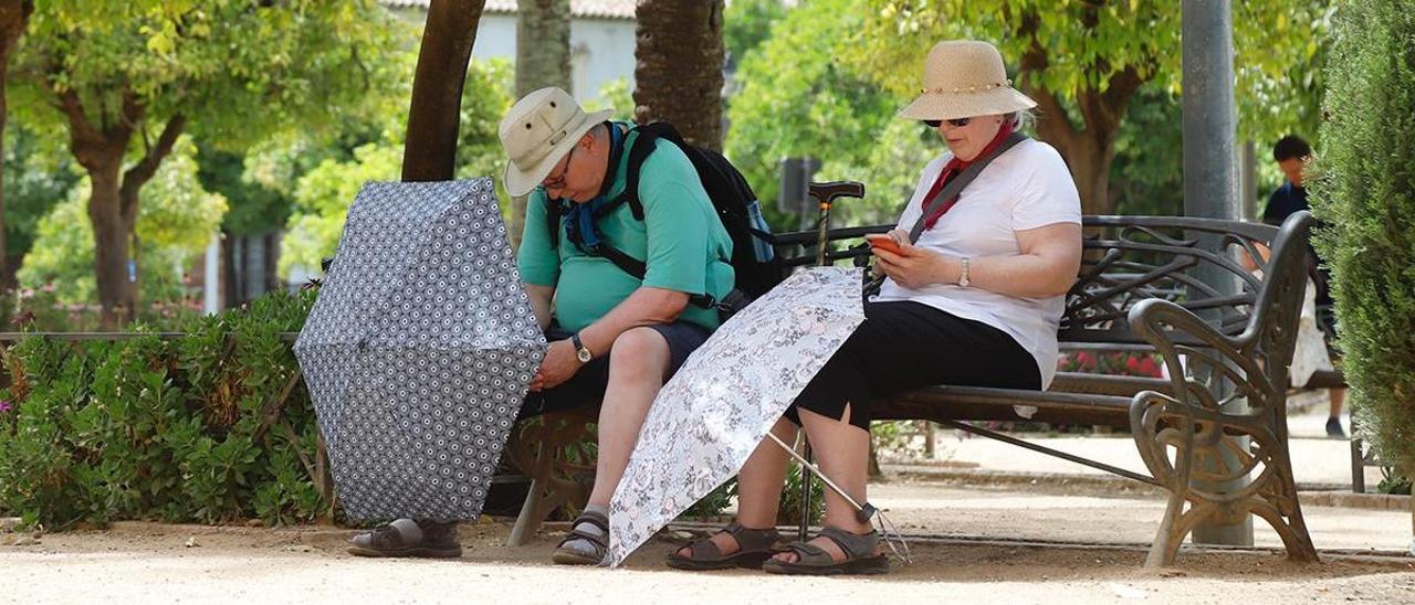 Dos personas se alivian del calor cordobés con sombreros y paraguas.