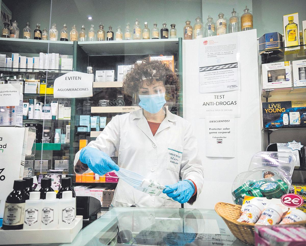 Una farmacéutica, totalmente protegida, prepara unas mascarillas para su venta en una botica de Zaragoza