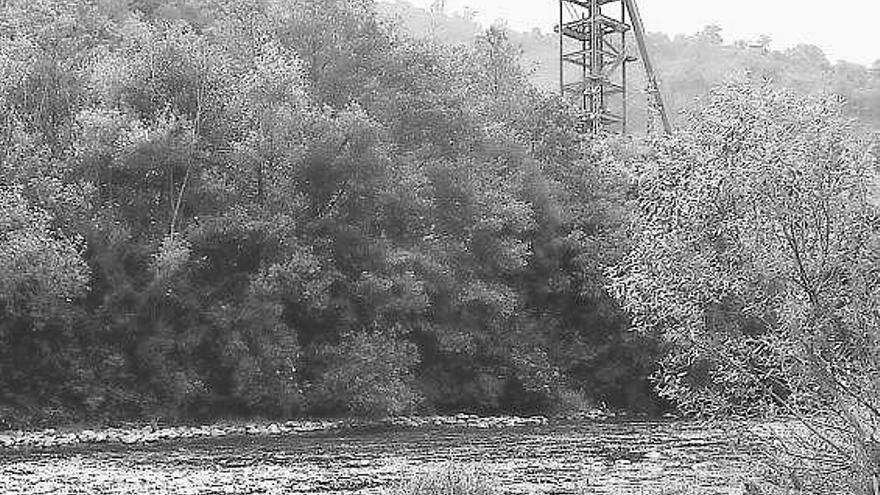 Las aguas del río Nalón, con el castillete del pozo minero Carrio detrás.