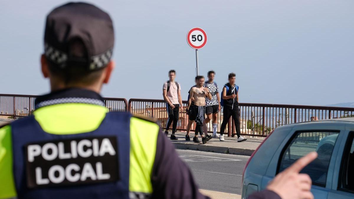 Un agente de la Policía Local de Alicante, con un grupo de jóvenes al fondo de la imagen