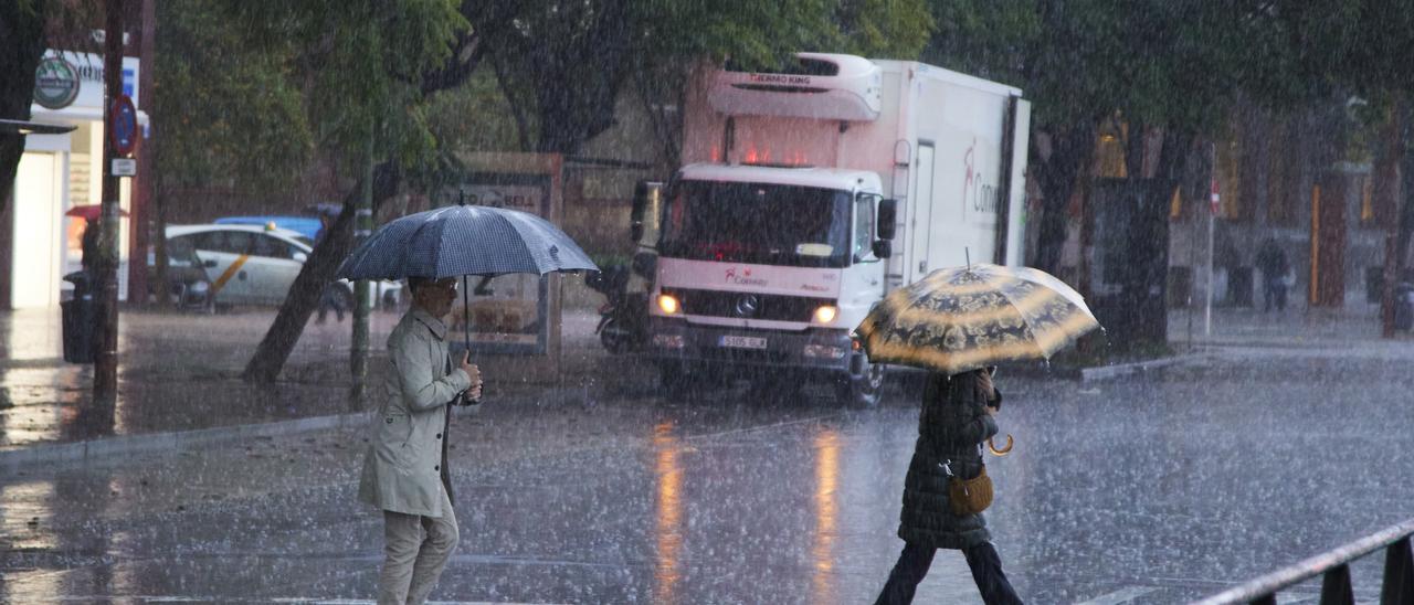 Dos mujeres cruzan bajo un paraguas un paso de peatones.