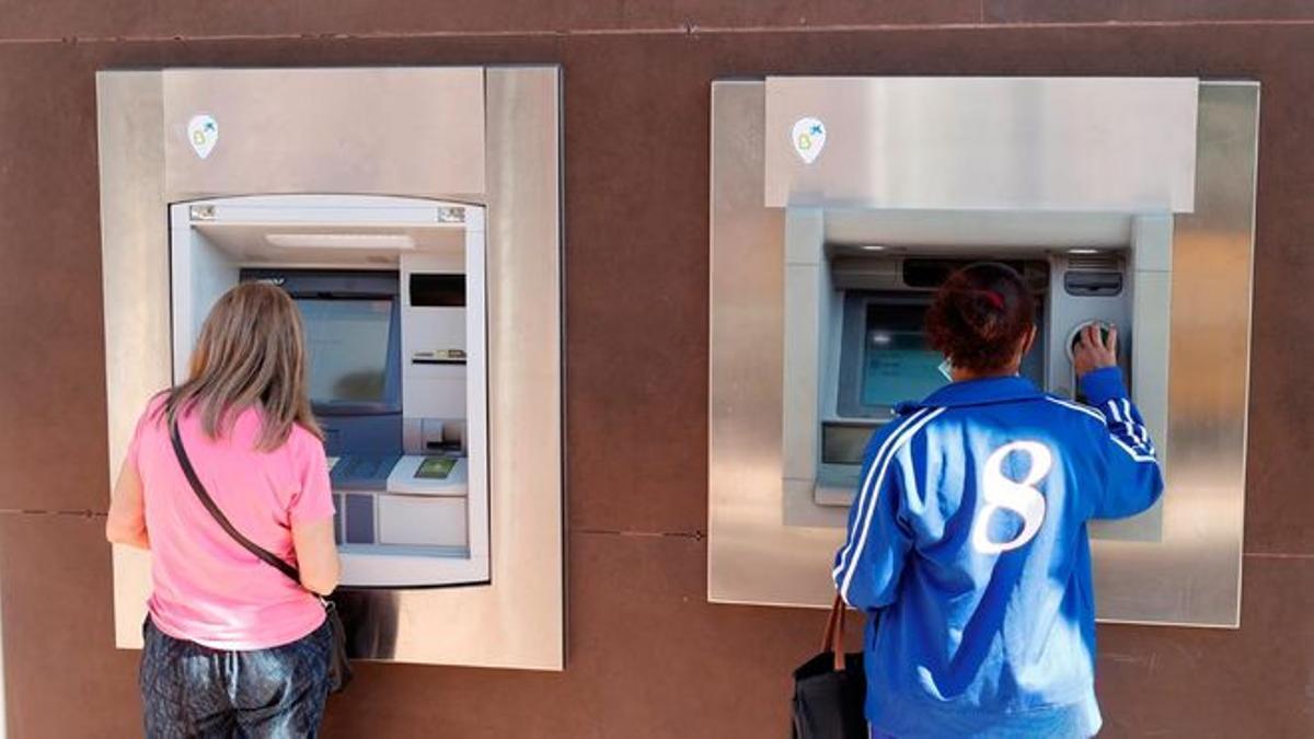 Dos personas sacan dinero de sendos cajeros automáticos en Madrid. / EFE