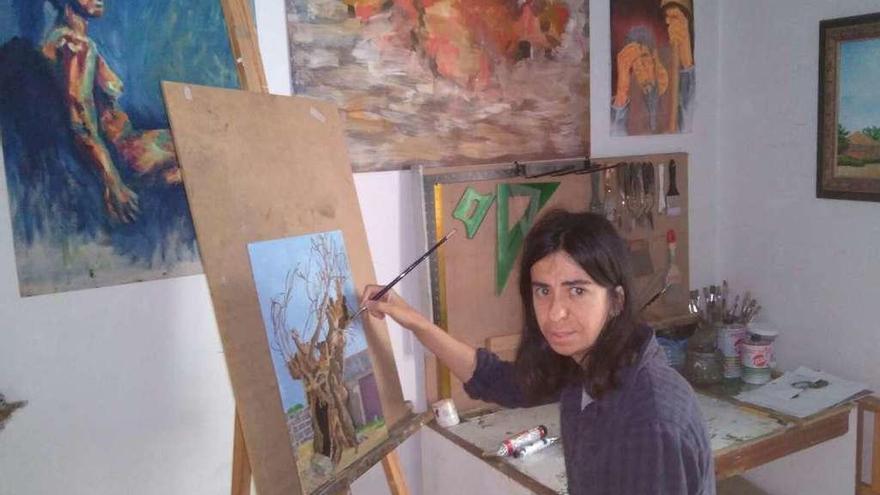 Susana Vega Carrasco en su estudio pintando un cuadro y rodeada de otras obras suyas.