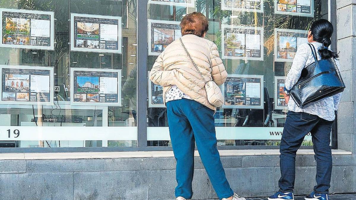 Dos personas observan el escaparate de una inmobiliaria.