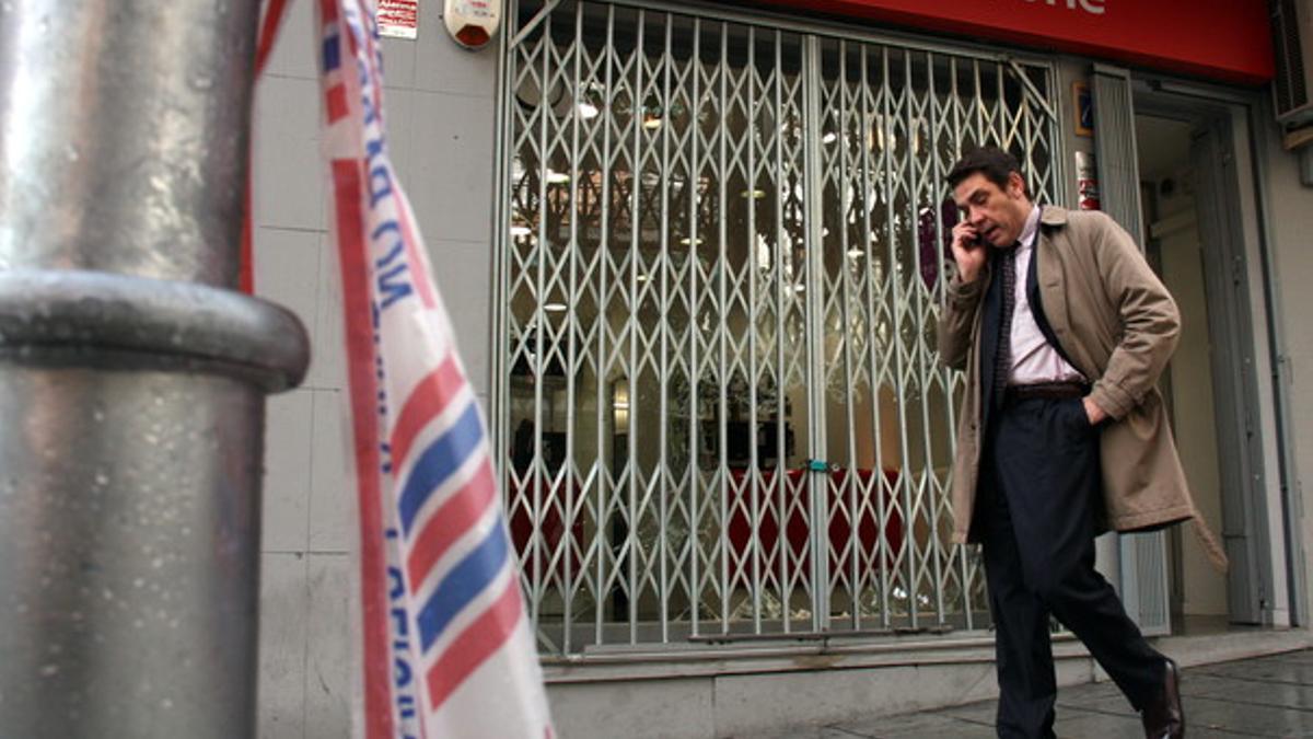 Un ciudadano habla por teléfono este miércoles al mediodía delante del escaparate destrozado de la tienda de telefonía móvil de la Rambla d'Anselm Clavé de Cornellà.