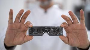 Un optometrista de la óptica Diferoptics, muestra unas gafas homologadas para la observación segura de eclipses solares