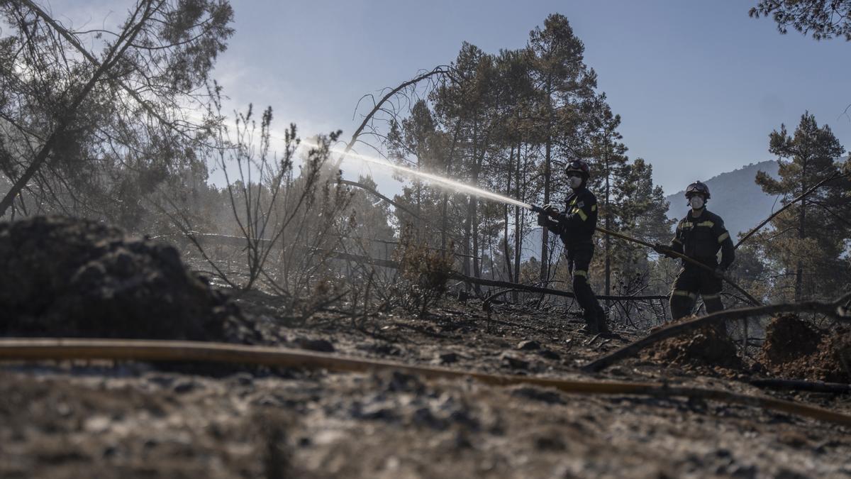 Efectivos de las brigadas forestales echan agua con una manguera durante los trabajos del incendio de Villanueva de Viver