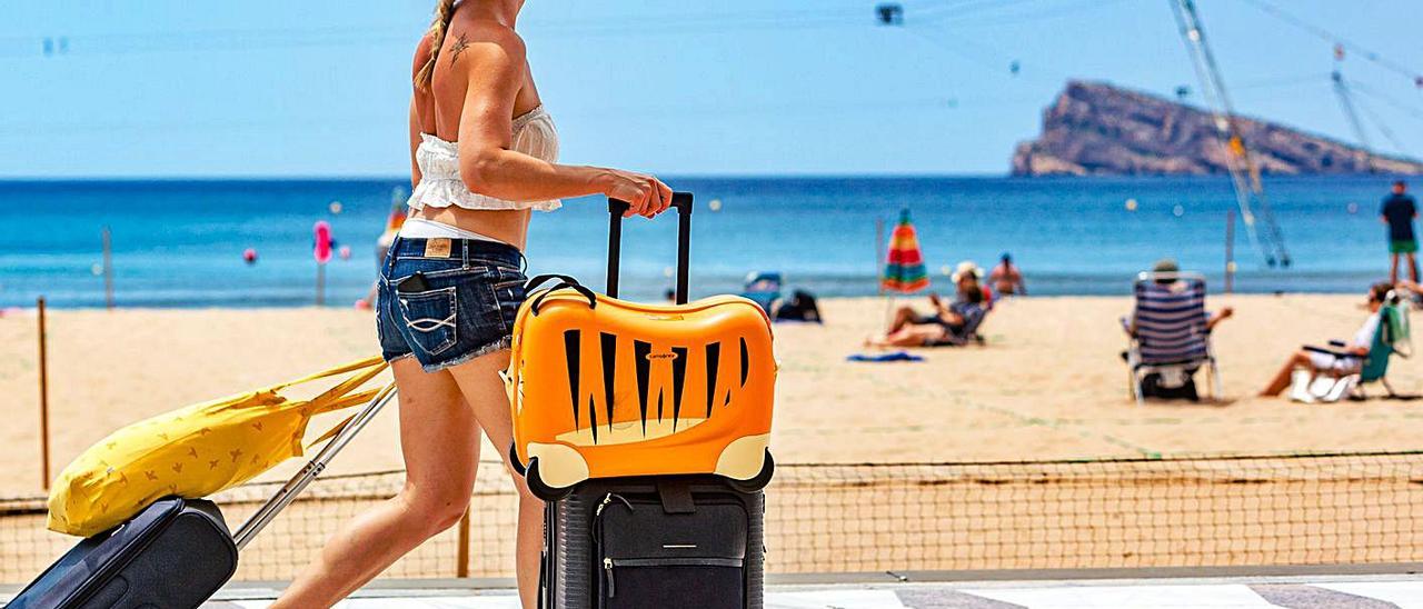 Una turista camina con sus maletas por el paseo de la playa de Levante de Benidorm. |