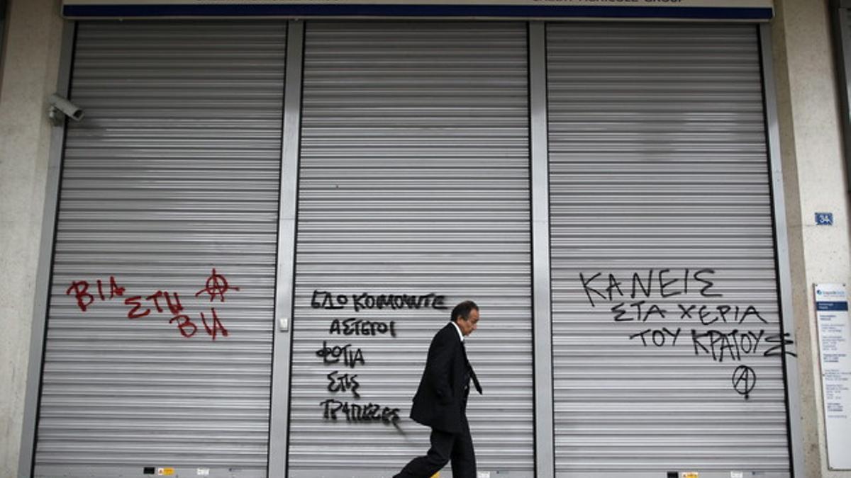 Un hombre camina junto a un banco cerrado en Atenas.