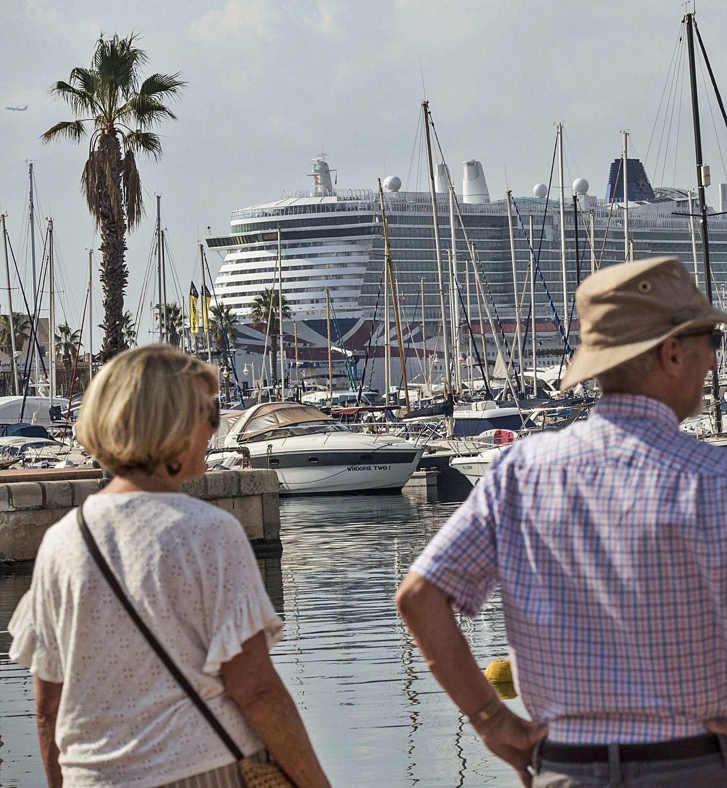 Dos cruceristas, pasajeros del «Iona», con la majestuosa imagen del barco al fondo. | 