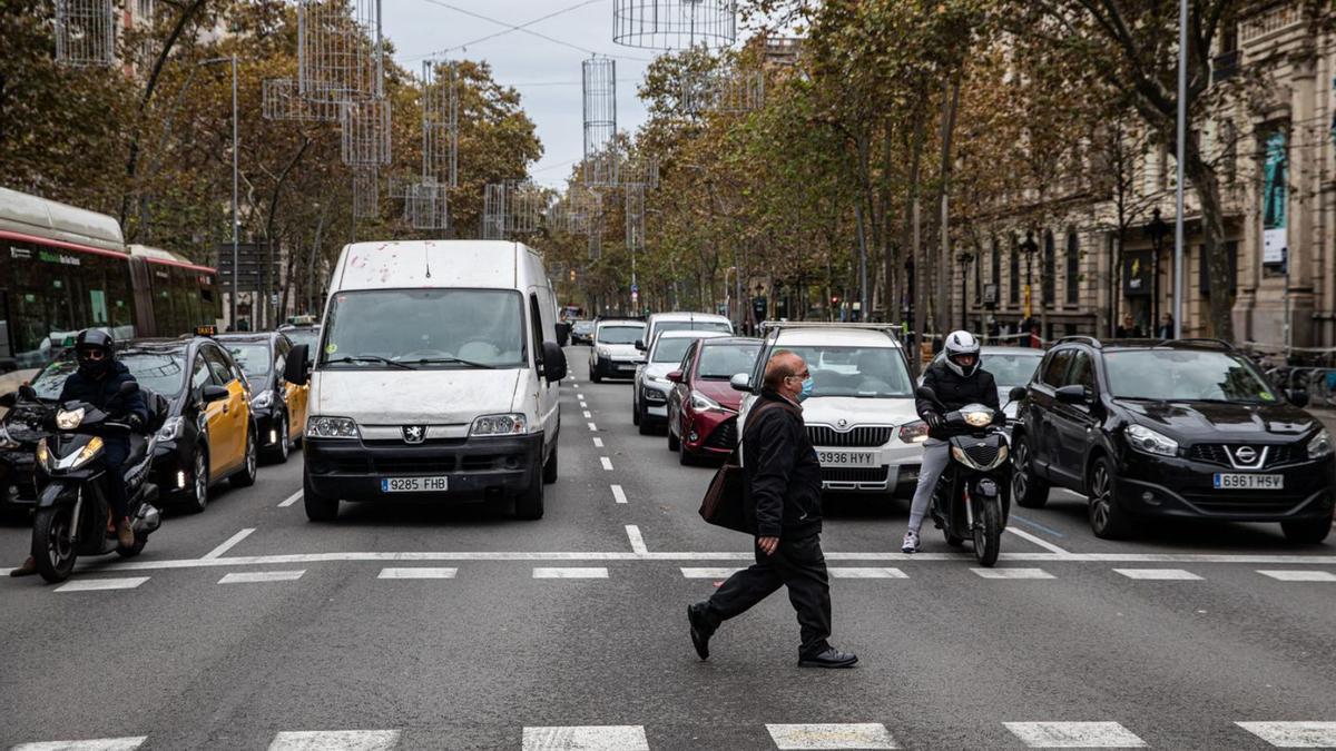 Un home amb mascareta creua per un pas de zebra davant de molts vehicles a Barcelona. | ZOWY VOETEN