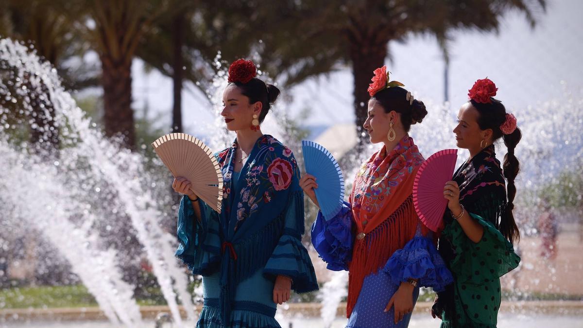 Tres jóvenes mujeres se abanican junto a la fuente de la portada de la Feria de Córdoba.