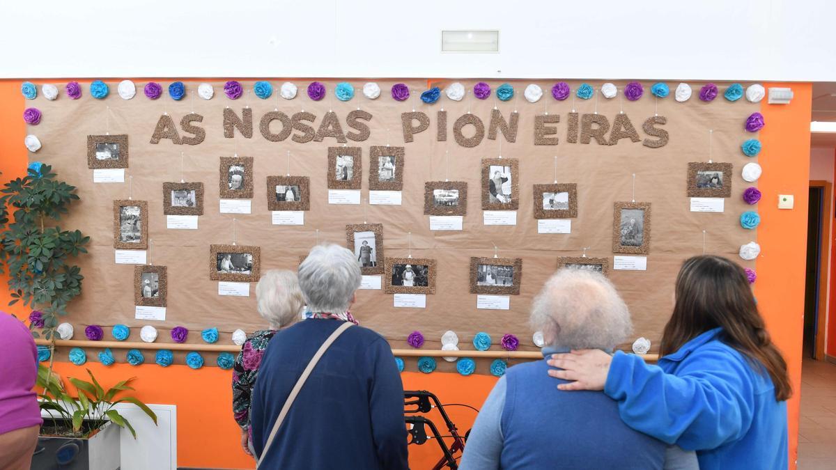 Usuarias y la educadora social del Centro de Día de Culleredo miran la exposición 'As nosas pioneiras'.