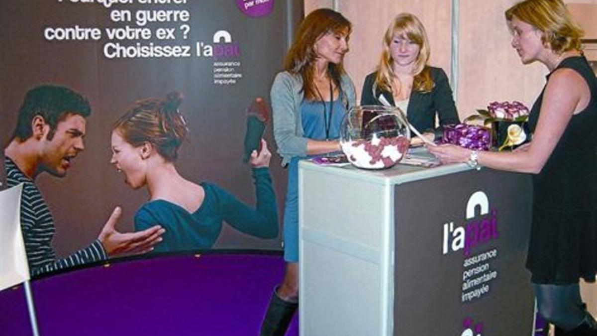 Tres mujeres, en un estand de una firma de seguros para pensiones alimentarias.