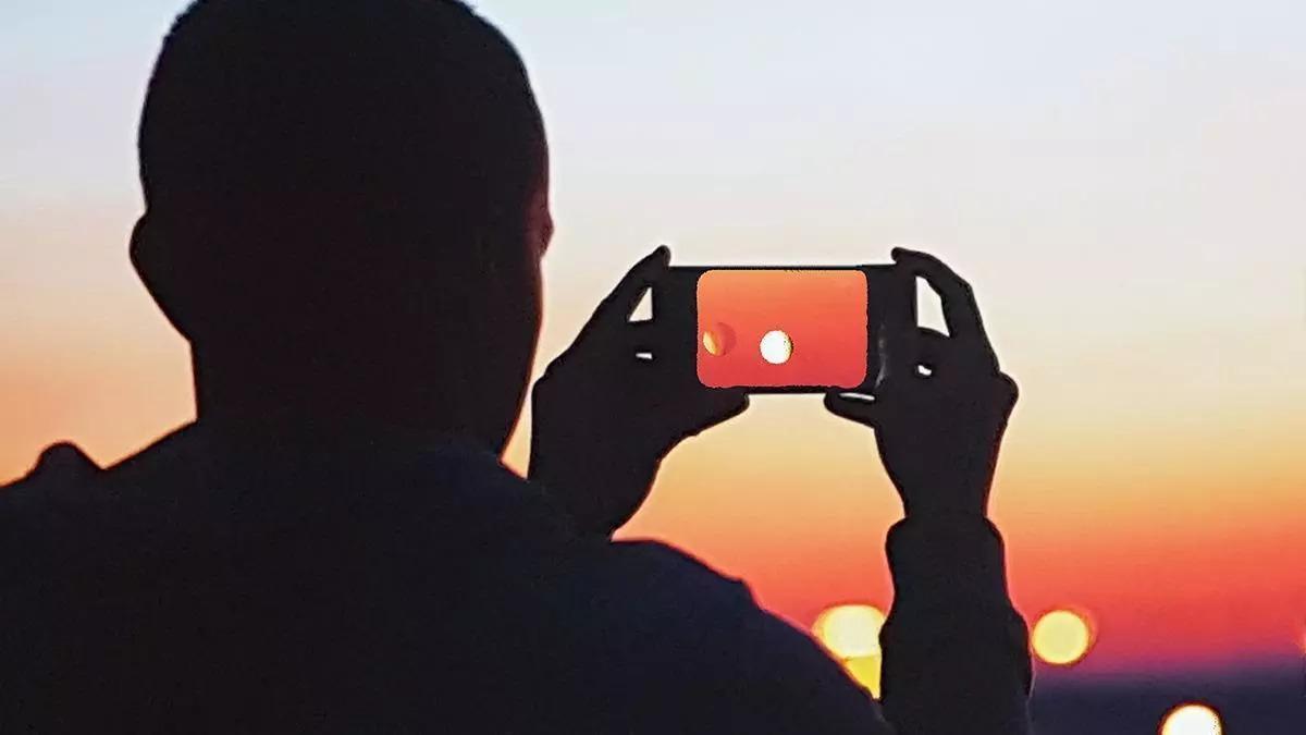 Un noi observa el Sol a través del seu telèfon mòbil