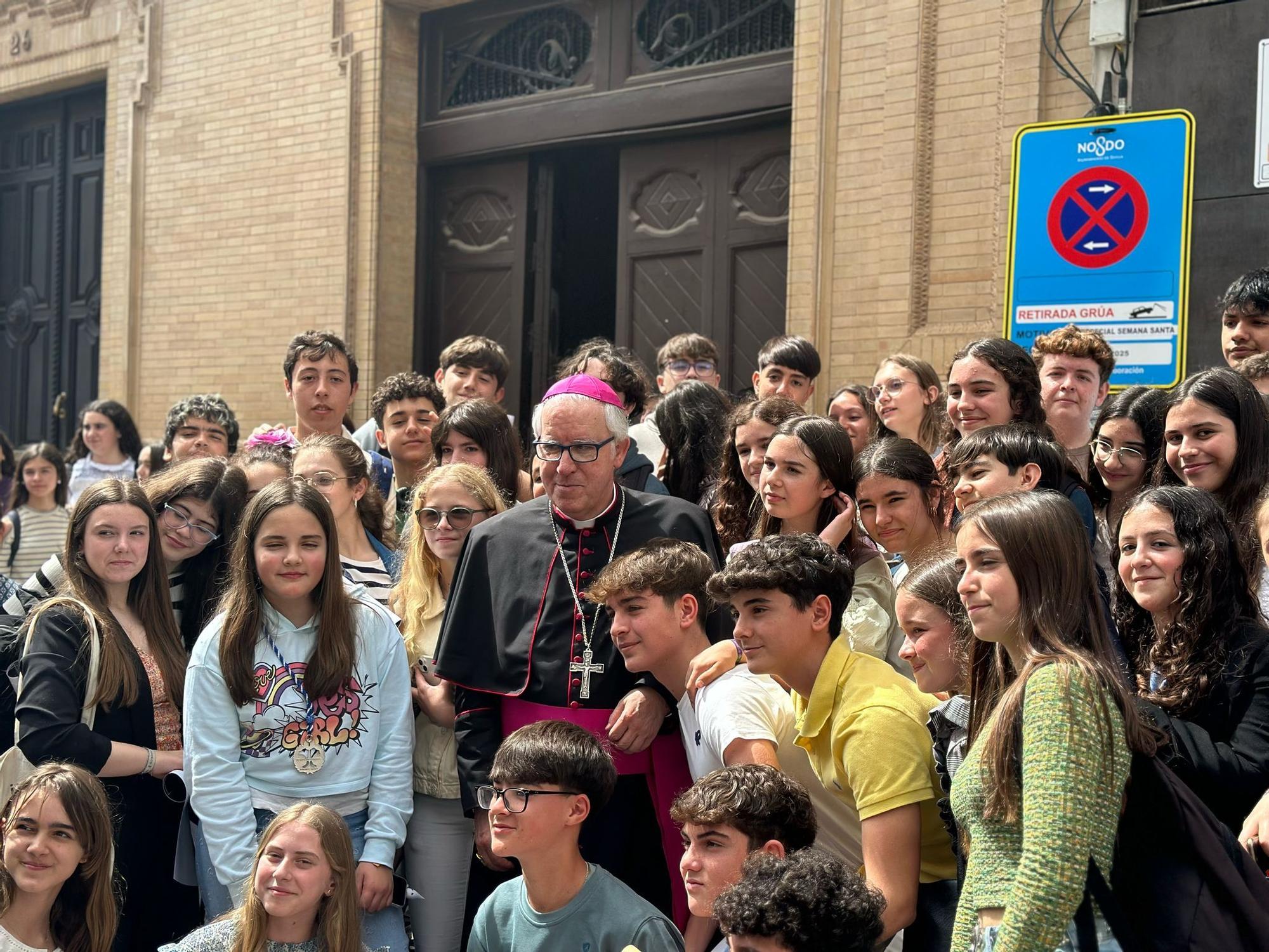 El arzobispo de Sevilla, Miguel Ángel Saiz, posa con los alumnos de un colegio de Morón de la Frontera a su entrada a la Parroquia de San Juan Bosco para ver el paso del Cristo de Pasión y Muerte.