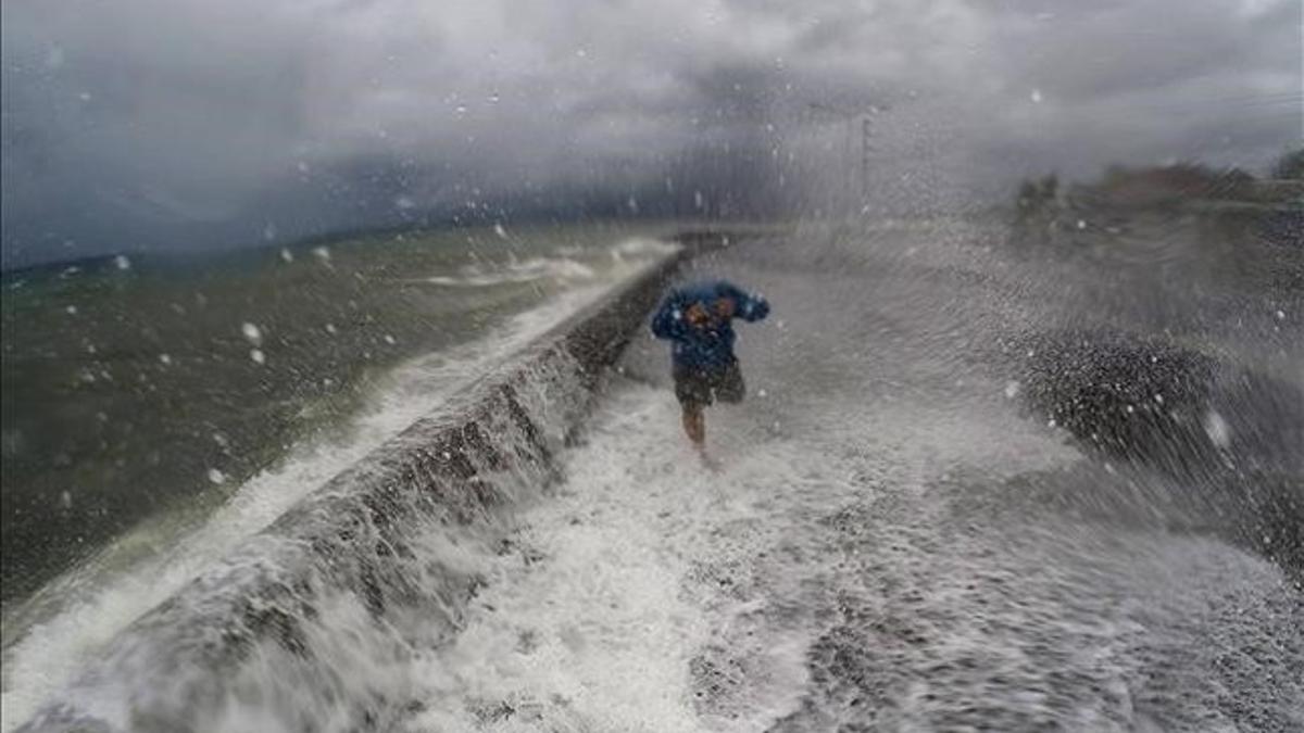 Un hombre pasa al lado de un muro superado por la olas en la ciudad de Legazpi, en el sur de Manila.