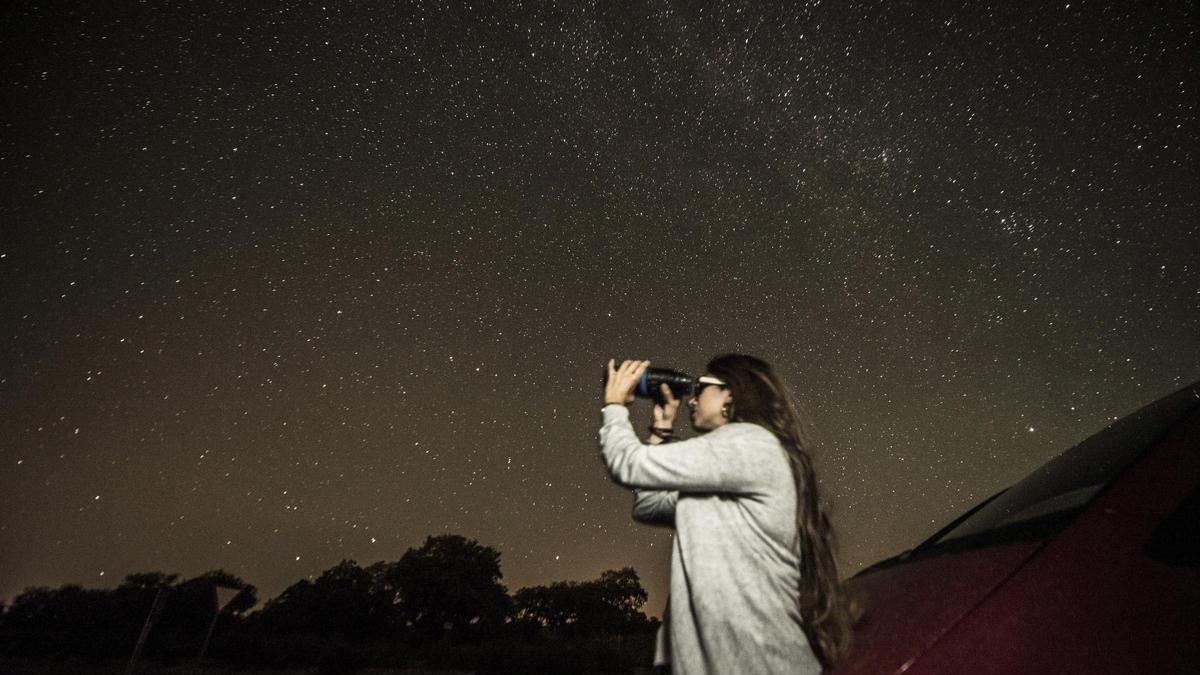 Una joven observa el cielo estrellado en un espacio rural.