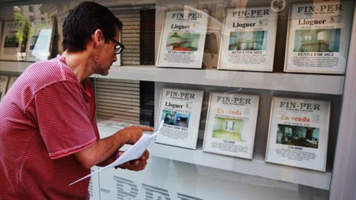 Un hombre mirando ofertas de pisos de alquiler en los expositores de una inmobiliaria del barrio del Poble Sec de Barcelona.