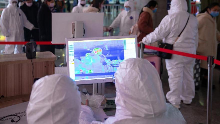 Personal médico con equipos de protección revisan la temperatura a los pasajeros en Nanjing, China.