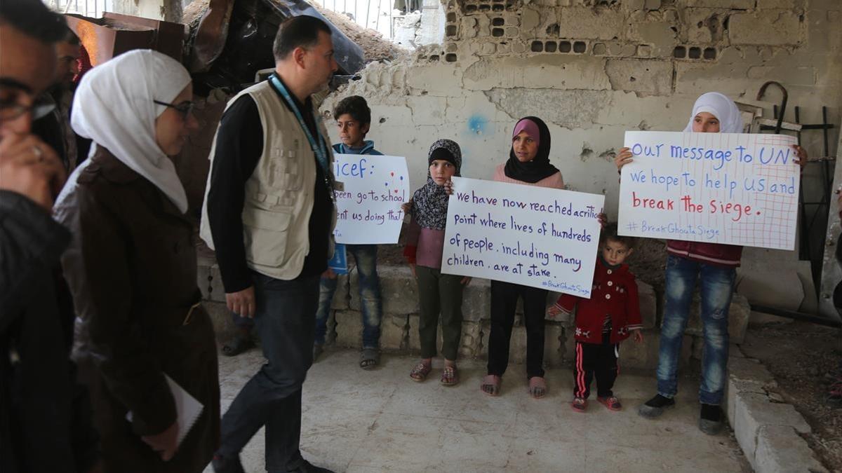 Niños sirios sostienen pancartas reivindicativas frente a miembros de un convoy de ayuda humanitaria durante una entrega de material en Al-Nashabia, en la región de Guta Oriental, al este de Damasco, el 28 de noviembre.