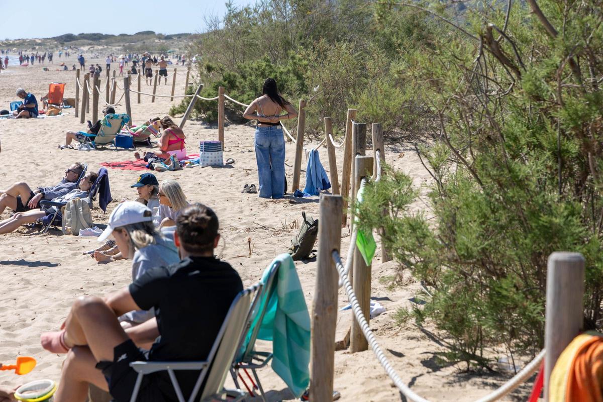 Usuarios en la playa del Carabassí junto al perímetro de vallado para evitar el acceso a las dunas