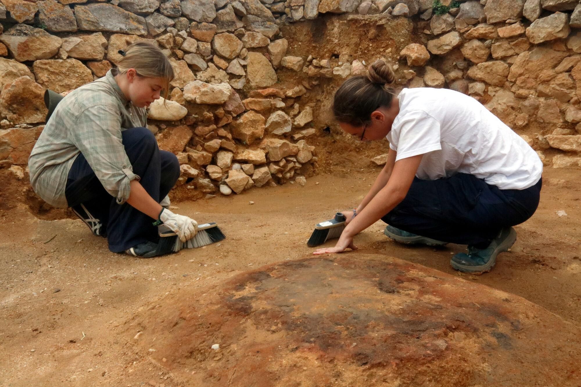 Dues arqueòlogues excavant una de les estances de la casa grega del segle V aC on s'ha trobat una llar de foc al centre