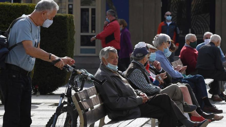 Varias personas descansan en un banco protegidos con mascarilla en León.