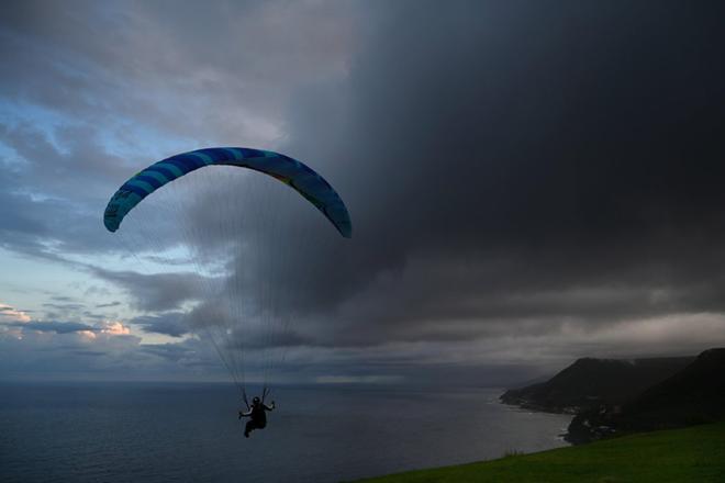 Un parapente sobrevuela al atardecer, mientras que las nubes de tormenta avanzan este jueves en Bald Hill, Nueva Gales del Sur, Australia.