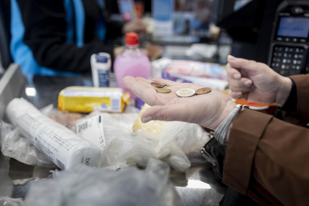 Una mujer cuenta las monedas de las que dispone para pagar la compra de alimentos en un supermercado.