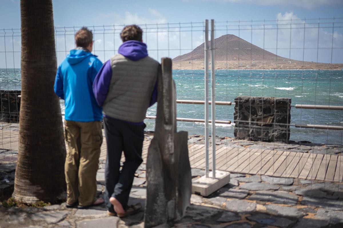 Dos turistas observan el oleaje tras unas vallas.