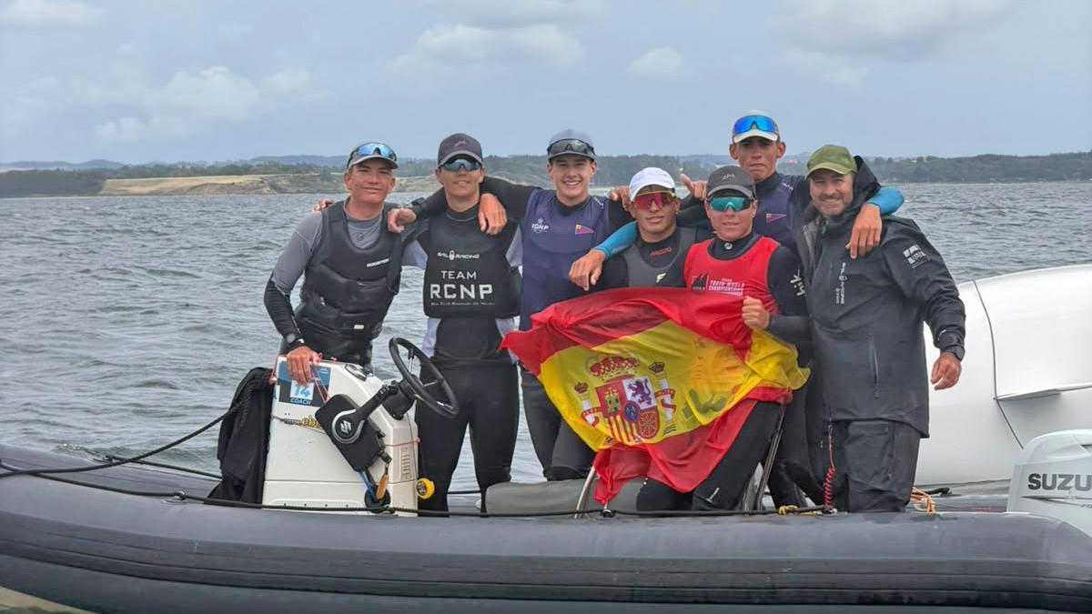 ikko Palou Espinar, con licra roja, celebra su éxito mundial con una bandera española junto a su entrenador y compañeros