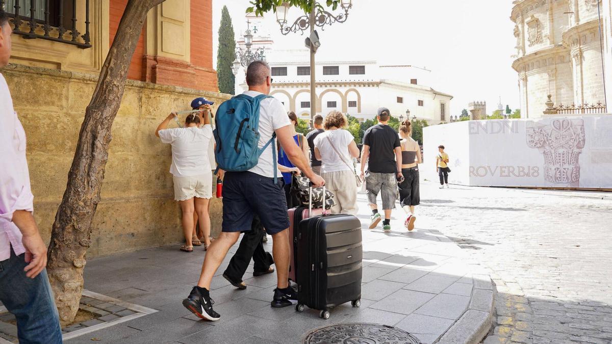 Turistas caminando por una calle del centro de Sevilla con maletas.