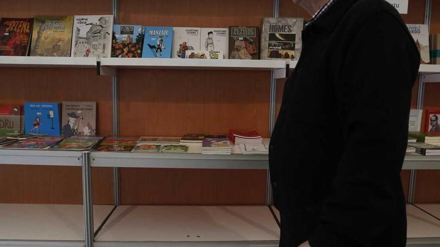 Un hombre pasa por delante de una estantería llena de libros en asturiano, ayer, al inicio de la feria.