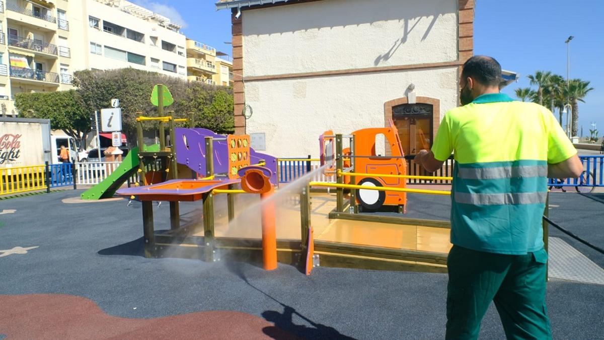 Un operario riega un parque infantil en  Rincón de la Victoria.