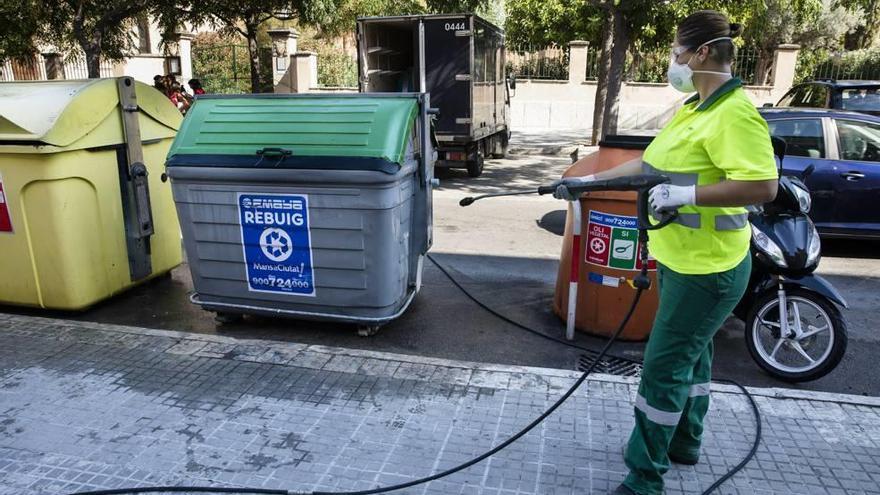 Una trabajadora de Emaya rocía con agua a presión un contenedor de basura en la calle Sant Magí.