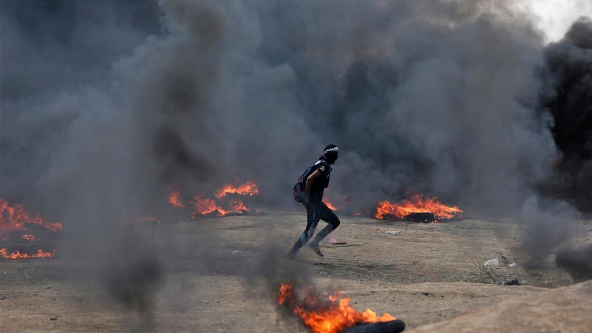 Un manifestante palestino corre entre las columnas de humo de neumáticos quemados en las protestas palestinas en la frontera de Gaza e Israel por el traslado de la embajada estadounidense a Jerusalén.