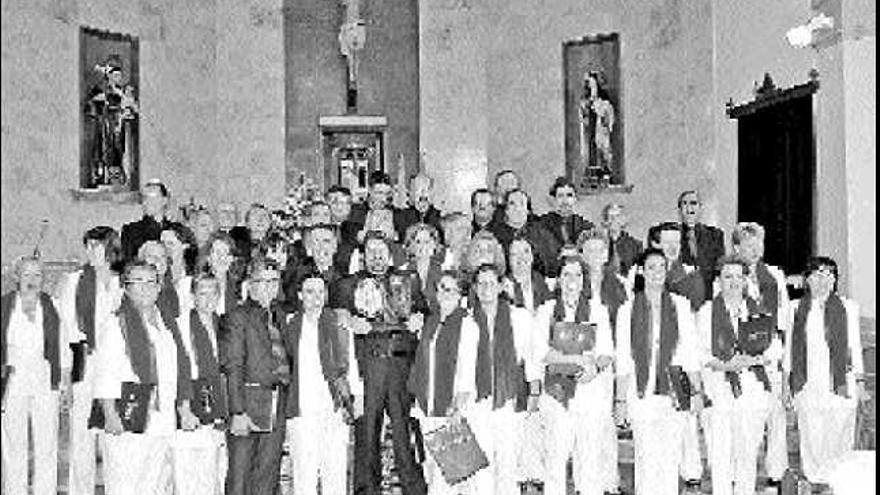 El coro ganador posa en la iglesia de Infiesto con su director, Javier Blanco Rubio, mostrando el trofeo.