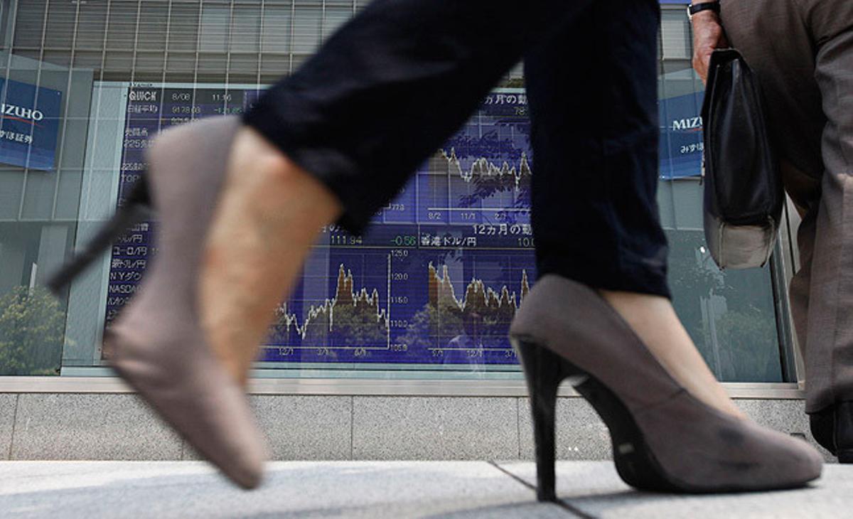 Una dona passa per davant d’una pantalla que mostra el tipus de canvi del ien respecte a altres monedes, en un carrer de Tòquio.