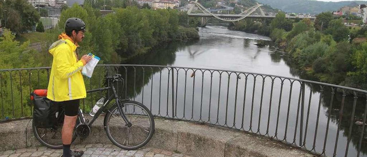 Un turista despliega un mapa en el Puente Romano de Ourense, ante el Miño, y el Puente del Milenio al fondo. // Iñaki Osorio