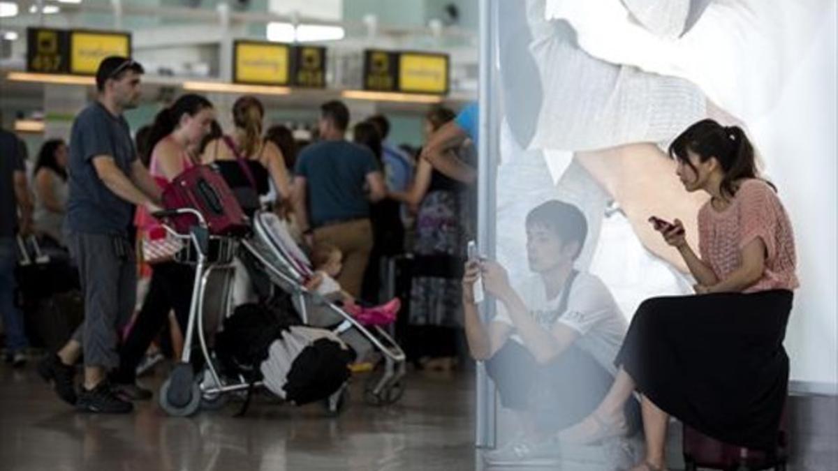 Unos pasajeros consultan sus 'smartphones' en el aeropuerto de El Prat, este verano.