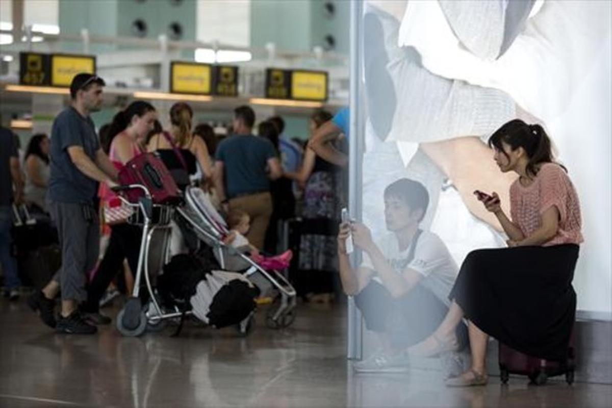 Uns passatgers consulten els seus ’smartphones’ a l’aeroport del Prat, aquest estiu.