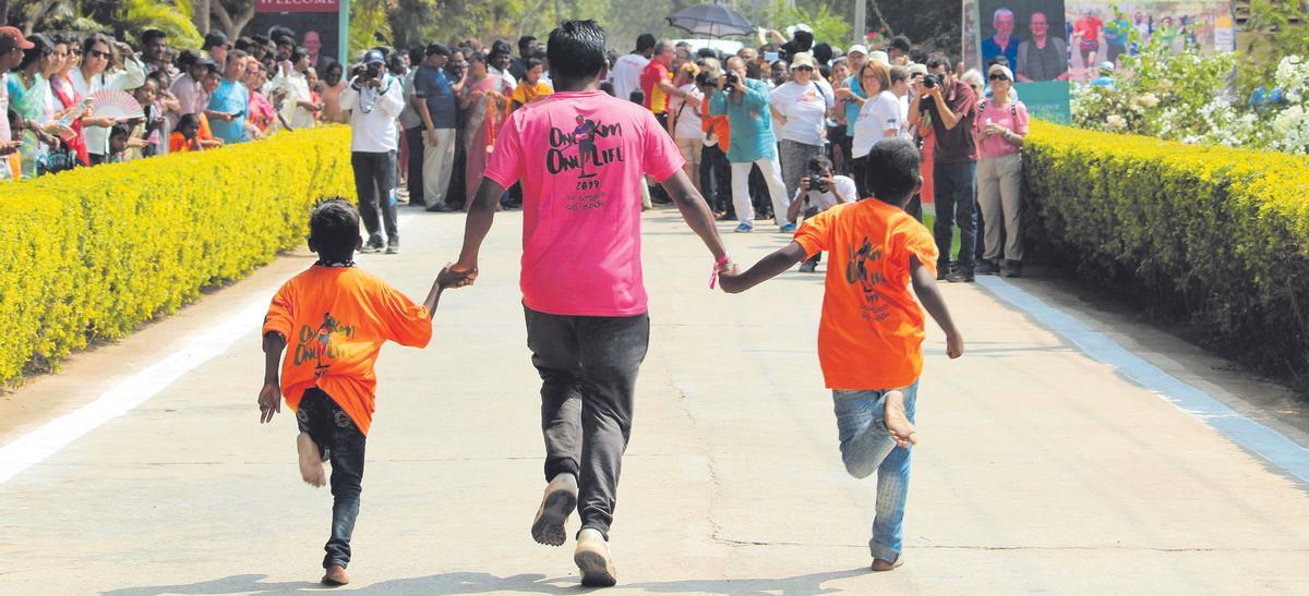 Un adulto y dos niños con la camiseta de la iniciativa ‘1km 1vida’ alcanzan la línea de meta de la carrera solidaria.