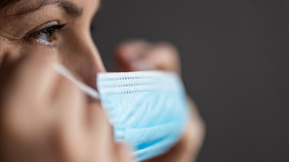 Una mujer se coloca una mascarilla.