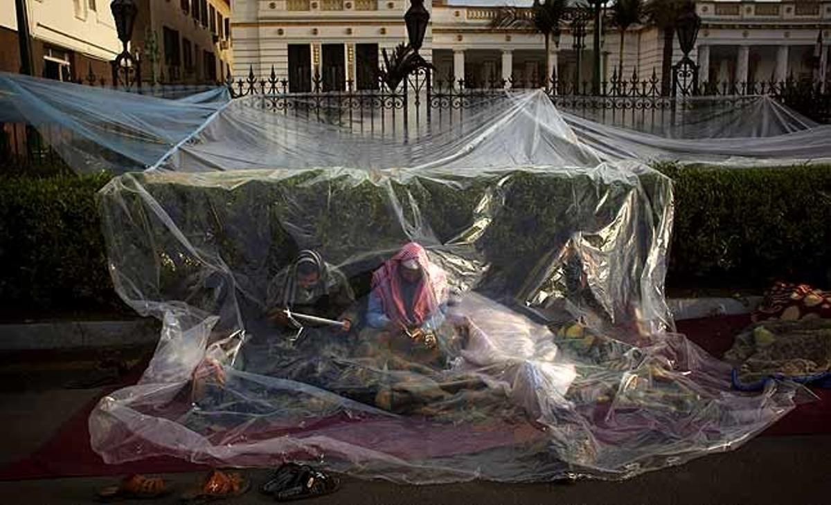 Manifestants en contra del govern egipci s’asseuen darrere d’un plàstic, després de passar la nit davant del Parlament egipci al Caire (Egipte).