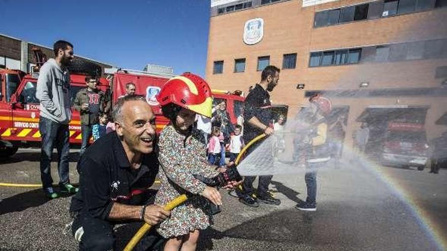 A la izquierda, Deva Fanjul, divirtiéndose con casco y manguera. En el centro, un grupo de niños, y a la derecha, dos bomberos dándoles explicaciones.